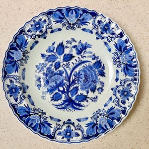 Può includere: Un piatto in ceramica bianca con un design floreale blu. Il piatto ha un bordo smerlato e un motivo floreale centrale. Lo schema di colori blu e bianco conferisce al piatto un aspetto classico ed elegante. Il piatto è adatto per servire cibo.