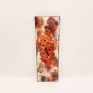 May include: A rectangular wall plaque featuring a textured, mottled brown and cream background. A vertical cluster of raised, circular elements in vibrant shades of orange, red, and yellow is centered on the surface, creating a layered, dimensional effect.