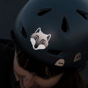 Peut inclure: Un casque de vélo bleu foncé avec un autocollant de loup blanc et d'autres petits autocollants. Le casque a plusieurs évents d'aération.