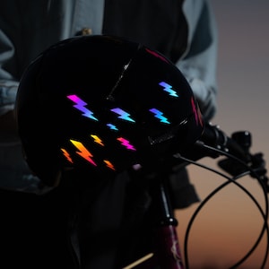 May include: A black bicycle helmet with a rainbow lightning bolt pattern. The helmet is being held by a person.