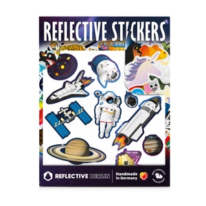 Könnte beinhalten: Eine Bogen mit reflektierenden Aufklebern mit Weltraum-Motiven, darunter eine Rakete, ein Astronaut, ein Raumschiff und Planeten. Die Aufkleber sind handgefertigt in Deutschland und tragen den Text "Reflective Berlin".