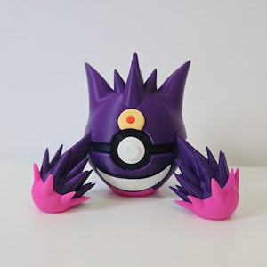 May include: A purple spherical figure with a wide white grin, featuring a black band across the center with a white circular button. The figure has pointed spikes on top, two large spiky purple arms with bright pink tips, and a yellow circular emblem with a red center on its forehead.