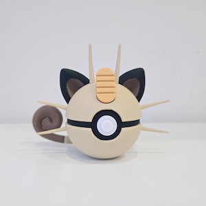 May include: A tan and black 3D-printed figure of a Pokémon character. The figure has a spherical body with a black stripe, a white button, and tan whiskers. It features black ears, a wooden-colored forehead piece, and a curled tail.
