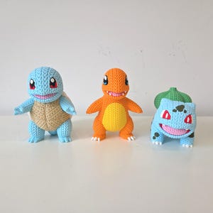 May include: Three handmade crochet figures of popular characters. A blue Squirtle with a tan shell, an orange Charmander, and a blue Bulbasaur with a green bulb on its back. Each figure has a unique design and expression.