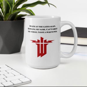 May include: White ceramic coffee mug with a red and black logo and the text "DEATH AT THE GATES AGAIN. HOWLING MY NAME. CAN'T GREET YOU TODAY. I HAVE A WAR TO WIN."