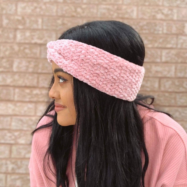 A woman with long black hair faced to the side wearing a soft velvet textured pink crochet headband with a twist in the centre.