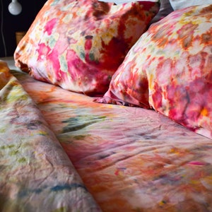May include: A bed with a colorful tie-dye duvet cover and two matching pillowcases. The duvet cover and pillowcases feature a mix of pink, orange, yellow, and green colors.