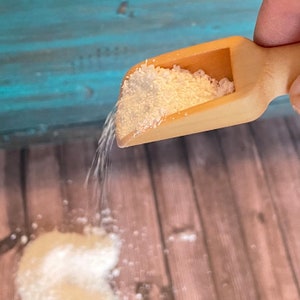 May include: A wooden scoop filled with white powder is being poured onto a wooden surface. The powder is spilling out of the scoop and forming a small pile on the surface.