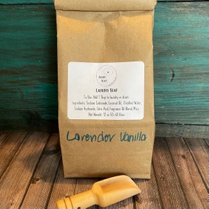 May include: A brown paper bag with a white label that reads "Laundry Soap" and lists the ingredients and instructions for use. The bag is labeled "Lavender Vanilla" and has a small wooden scoop next to it.