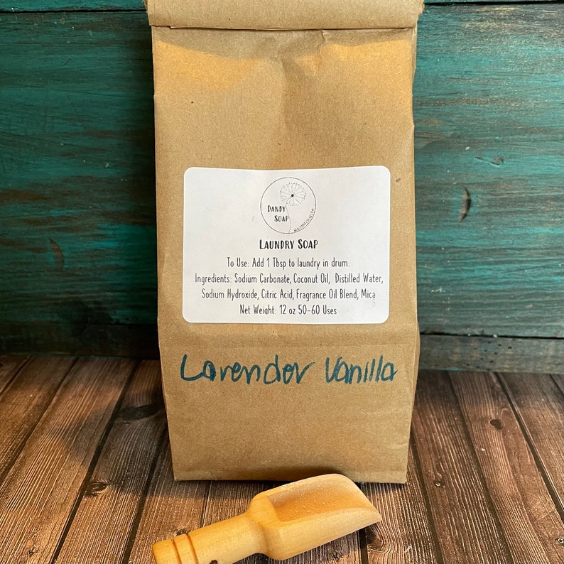 May include: A brown paper bag with a white label that reads "Laundry Soap" and lists the ingredients and instructions for use. The bag is labeled "Lavender Vanilla" and has a small wooden scoop next to it.