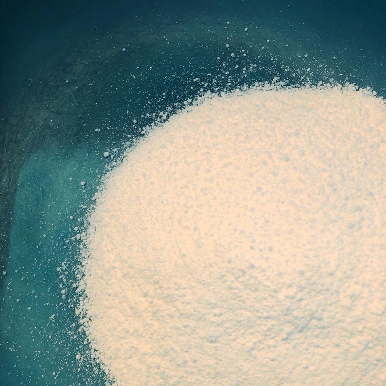 May include: A close-up of a white powder in a blue bowl. The powder is spread out evenly and has a fine texture.