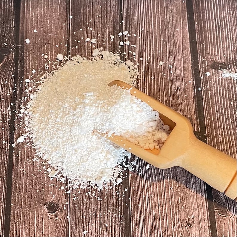 May include: A white powder, possibly baking soda or cornstarch, is piled on a wooden surface. A small wooden scoop is partially filled with the powder and rests on top of the pile.