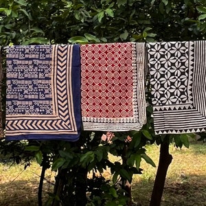 K&ouml;nnte beinhalten: F&uuml;nf verschiedene gemusterte Stoffquadrate h&auml;ngen an einer W&auml;scheleine. Die Quadrate sind alle in Blaut&ouml;nen, Schwarz, Wei&szlig; und Braun gehalten. Die Muster umfassen Sterne, geometrische Formen und Blumenmuster.