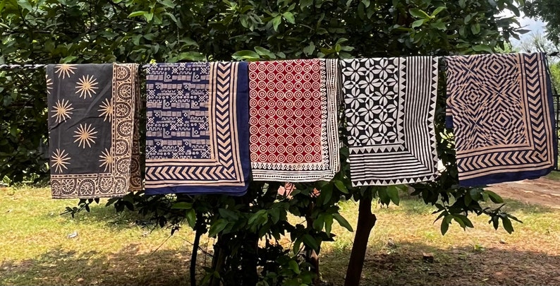 K&ouml;nnte beinhalten: F&uuml;nf verschiedene gemusterte Stoffquadrate h&auml;ngen an einer W&auml;scheleine. Die Quadrate sind alle in Blaut&ouml;nen, Schwarz, Wei&szlig; und Braun gehalten. Die Muster umfassen Sterne, geometrische Formen und Blumenmuster.