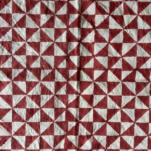 K&ouml;nnte beinhalten: Ein wei&szlig;er Stoff mit einem sich wiederholenden Muster aus roten Dreiecken. Die Dreiecke sind in einem Gittermuster angeordnet, wodurch ein geometrisches Design entsteht.