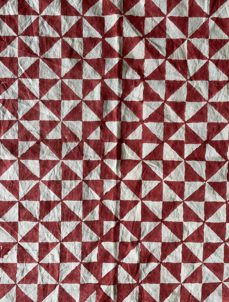 K&ouml;nnte beinhalten: Ein wei&szlig;er Stoff mit einem sich wiederholenden Muster aus roten Dreiecken. Die Dreiecke sind in einem Gittermuster angeordnet, wodurch ein geometrisches Design entsteht.