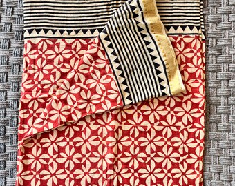 May include: A red and white cotton fabric with a geometric pattern. The fabric has a gold border with black and white stripes.