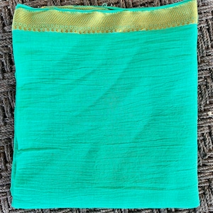 May include: A folded, turquoise fabric with a gold-colored border. The fabric has a textured appearance and is neatly folded. The gold border features a detailed pattern. The overall presentation suggests a textile product, possibly a scarf or shawl.