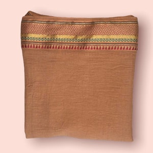 May include: A brown fabric rectangle with a decorative border. The border is made of gold, green, and red thread and features a repeating diamond pattern.