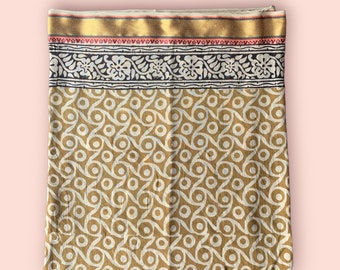 May include: A gold and white cotton fabric with a repeating pattern of circles and swirls. The fabric has a border with a floral design in black and white.