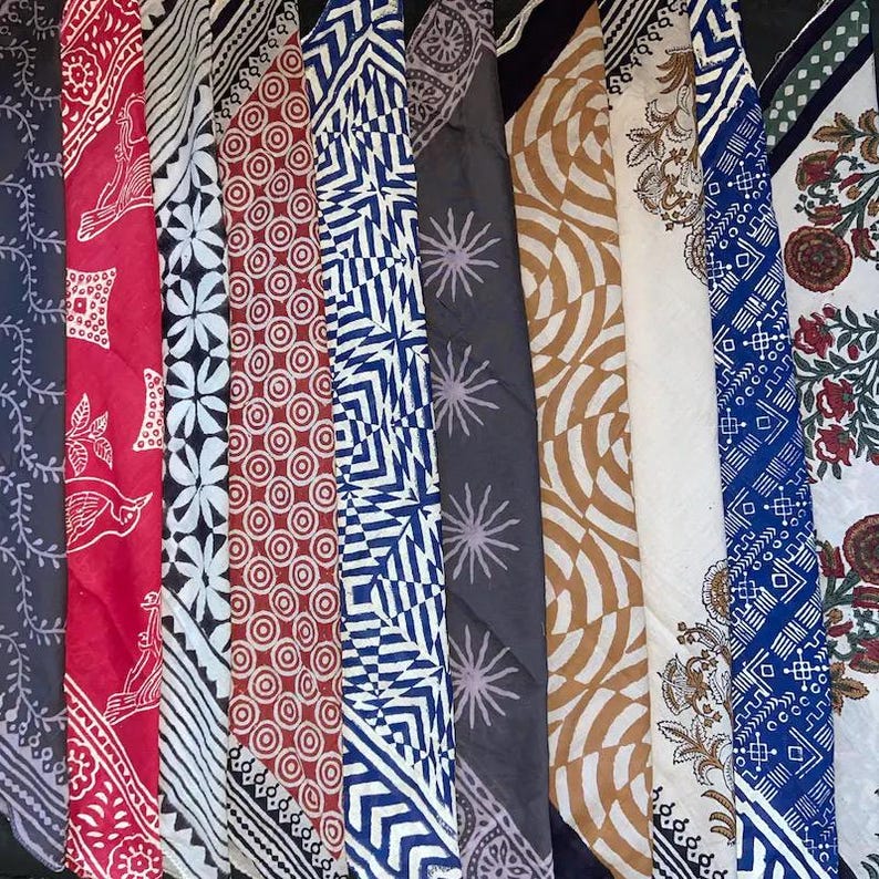 K&ouml;nnte beinhalten: Eine Sammlung von zehn bunten Stoffquadraten mit verschiedenen geometrischen und floralen Mustern. Die Quadrate sind in einer Reihe angeordnet, wobei die Oberkante jedes Quadrats ausgerichtet ist. Die Stoffquadrate sind alle in verschiedenen Farben, darunter Rot, Blau, Gr&uuml;n und Wei&szlig;.