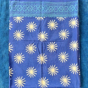 Può includere: Un tessuto di cotone blu con un motivo a stella bianca. Il tessuto ha un bordo blu e verde con un design geometrico.
