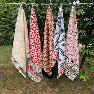 Könnte beinhalten: Vier Baumwollschals mit verschiedenen Mustern und Farben hängen an einer Wäscheleine. Die Schals sind in Rot-, Weiß-, Blau- und Brauntönen gehalten. Die Schals sind alle handbedruckt mit aufwendigen Designs.