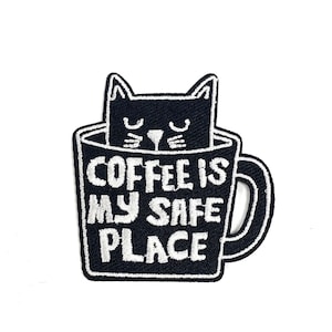 May include: Black and white embroidered patch of a cat inside a coffee mug with the text "Coffee is my safe place".