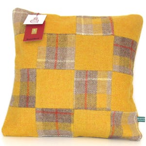 May include: Square decorative pillow with a patchwork design. The pillow features a vibrant yellow background with squares of gray and yellow plaid fabric. A red tag is attached to the pillow. The pillow is a home decor item.