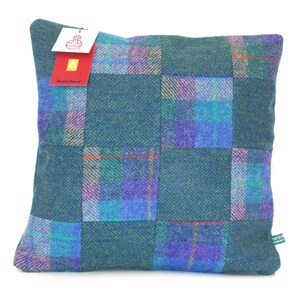 May include: Square decorative pillow with a patchwork design in shades of teal, purple, and blue. The pillow features a mix of plaid and herringbone patterns. A tag with the text "Harris Tweed" is attached.