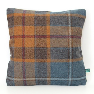 May include: Square decorative pillow with a plaid pattern in shades of blue, brown, orange, and red. The pillow has a soft, textured appearance and a tag on the side. The pillow is a home decor item.