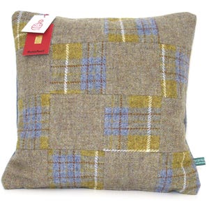 May include: Square decorative pillow with a patchwork design. The pillow features a tan background with blue, yellow, and white plaid squares. A red and white tag is attached to the pillow. The pillow is made of a textured fabric.