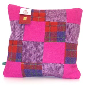 May include: A square decorative pillow with a patchwork design. The pillow features a vibrant mix of pink, red, purple, and plaid patterns. A tag is attached to the pillow. The pillow is made of a soft, textured fabric.
