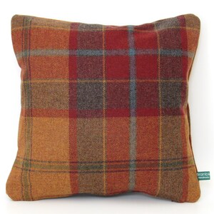 May include: Square decorative pillow with a plaid pattern in shades of orange, red, brown, and blue. The pillow has a soft, textured appearance, suggesting a woven fabric. A small green tag with white text is visible on the side.