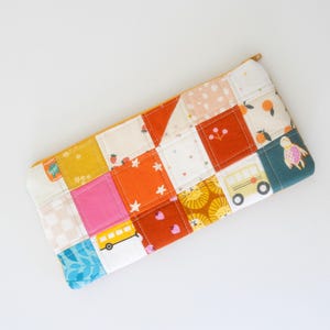 May include: A patchwork pencil case with a yellow zipper. The case is made of various fabric squares in colors like orange, pink, yellow, and teal. Some squares feature patterns of stars, strawberries, and a school bus.