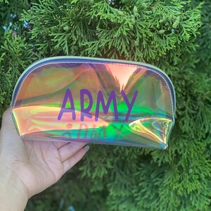 May include: A clear iridescent makeup bag with a zipper closure. The bag has the word "ARMY" printed in purple letters.