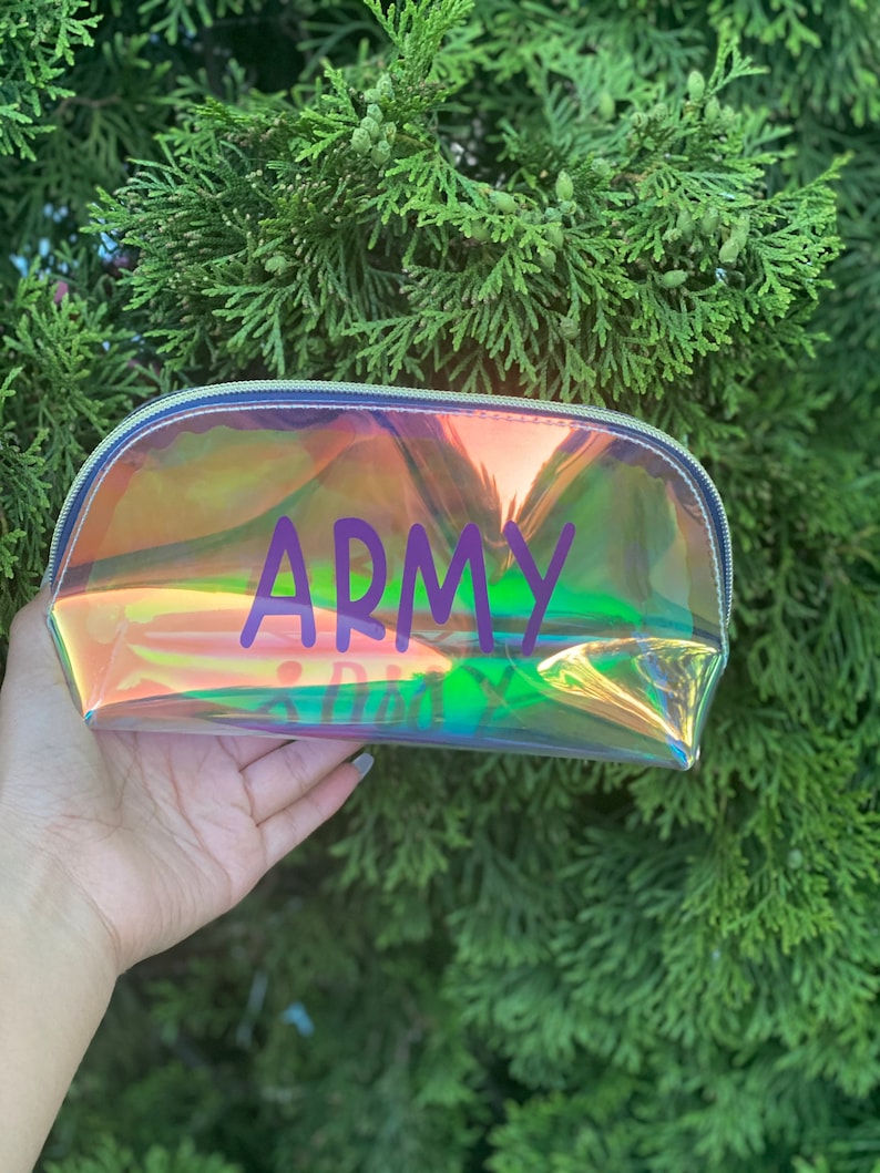 May include: A clear iridescent makeup bag with a zipper closure. The bag has the word "ARMY" printed in purple letters.