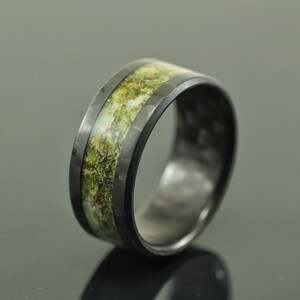 May include: A black carbon fiber ring with a green and white inlay. The ring has a hammered finish.