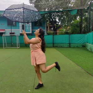 May include: A woman in a pink dress holds a black and white lace umbrella while standing on a green artificial grass field.