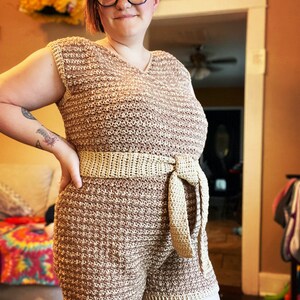 May include: A crocheted jumpsuit with a brown and cream color pattern. The jumpsuit has a wide, crocheted belt that ties at the front.