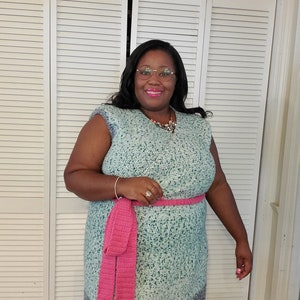 May include: A teal blue crochet dress with a pink crocheted belt. The dress has a sleeveless design and a slightly flared skirt.