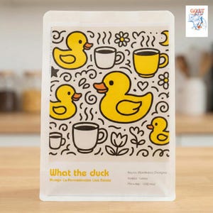 May include: A white coffee bag with a playful design of yellow ducks, coffee cups, and floral motifs. The text "What the duck" is in yellow, with details about the coffee's origin and variety. The bag has a fun, cartoonish style.