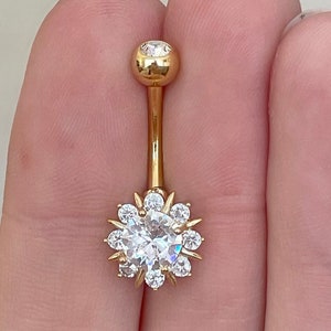May include: Gold belly button ring with a large clear crystal surrounded by smaller crystals in a flower shape.