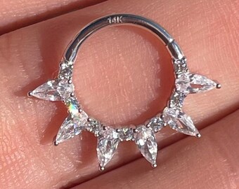 May include: A silver ring with a row of clear stones around the band and five larger clear stones that point outwards. The ring is marked "14K".