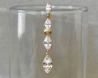 Peut inclure: Une boucle d'oreille dorée avec un long pendentif orné de cinq pierres de forme marquise transparentes.
