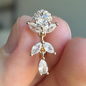 May include: Gold earring with a flower design featuring clear cubic zirconia stones.