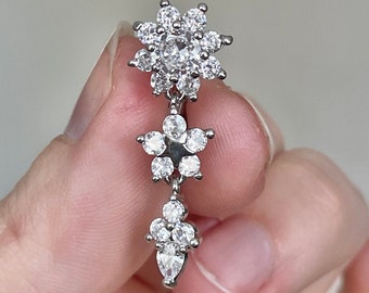 May include: Silver dangle earring with three flower-shaped clusters of clear cubic zirconia stones.