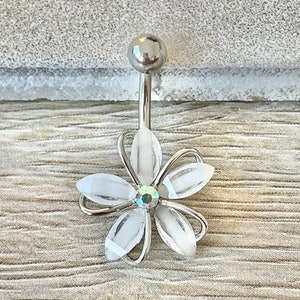 以下が含まれることがあります： 白い花チャームと中央にクリアなラインストーンが付いたシルバーのへそピアス