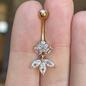 May include: Gold belly button ring with a clear crystal flower design. The flower has five petals and a center stone.