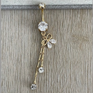 May include: Gold belly button ring with a clear crystal and a dangling chain with clear crystals and a bow charm.